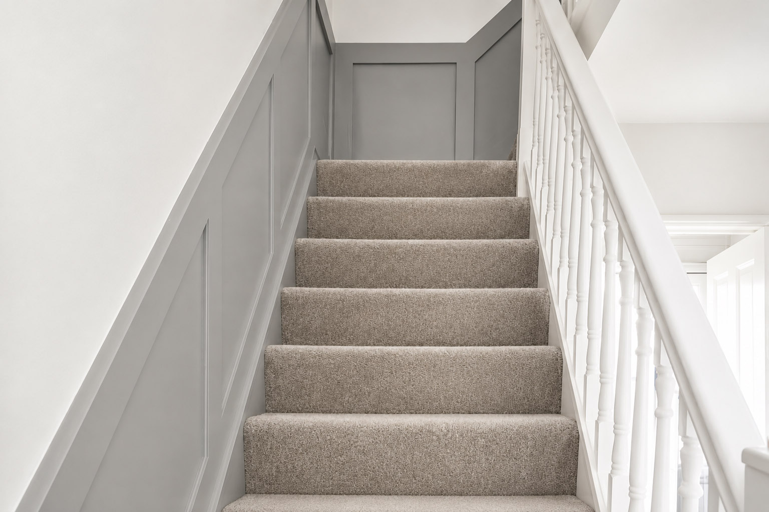 Completed grey staircase wall panelling with neutral carpet and white balustrade by Elite
